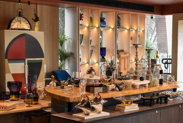 Interior of FabCuro, a home decor store in Bangalore’s Kasturi Nagar, featuring home decor items displayed on a wooden console and open shelving, including decorative sculptures, vases, glassware, lamps, mirrors, and accent pieces.